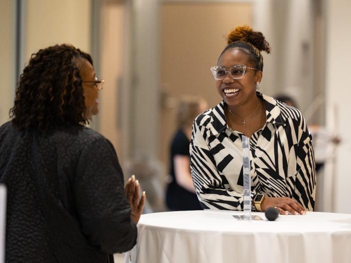 Women laughing while standing at a table at a SOM Diversity Mixer event.