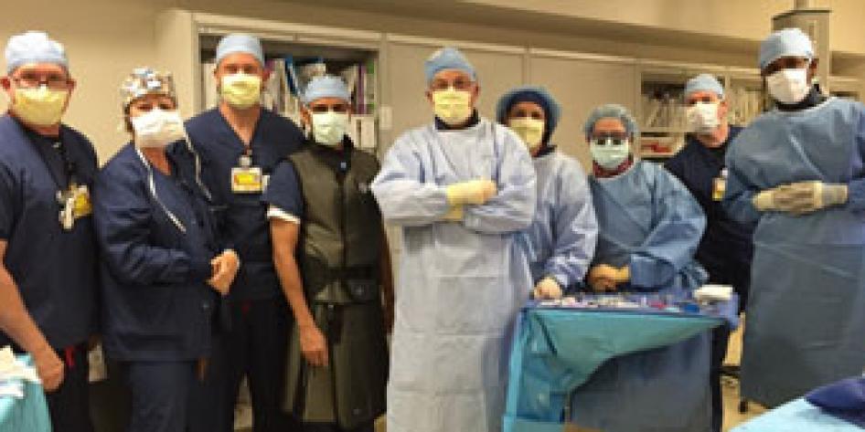 nine surgeons standing in OR theater in dark and light blue gowns