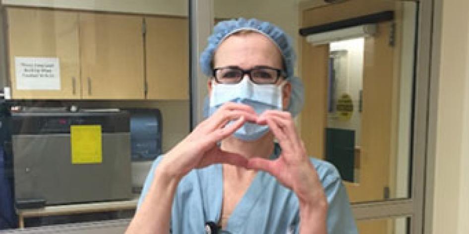 Beth McClusky, OR, RN in OR scubs in hospital setting, making shape of heart with her fingers.