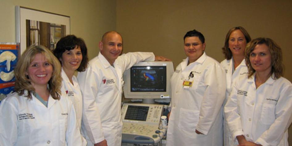 six surgeons wearing lab white coats in vascular lab surrounding diagnostic mashine in office setting