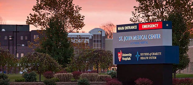University Hospitals St. John Medical Center with sign in foreground saying main entrance, emergency st. john medical center a catholic hospital, UH logo with Universersity Hospital text, and Sisters of Charity Health System with Logo, with building in background.