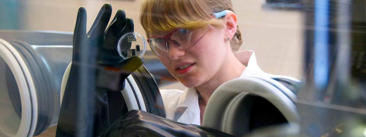 A woman in a lab wearing gloves and goggles, ready to conduct experiments.