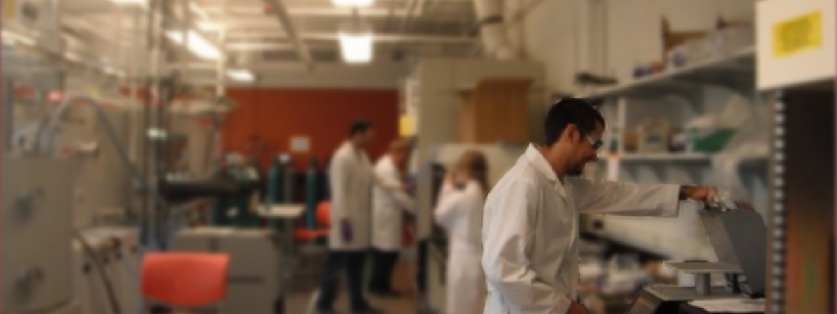 Multiple people in white lab coats working in a lab at various machines.