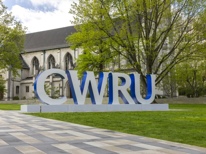 Silver and blue statue of the letters CWRU in front of a gothic revival chapel and tree