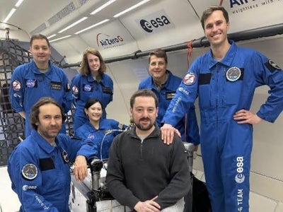 Ya-Ting Liao (pictured left) and other scientists and researchers wearing blue flight suits labeled “Zero-G-Team ESA” stand aboard an aircraft.