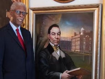 David A.G. Johnson Jr. standing in a suit next to a portrait of John Sykes Fayette.