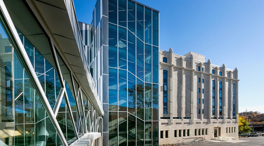 Modern glass building with angular design adjacent to a classic stone structure under clear blue sky, conveying contrast between contemporary and traditional architecture.