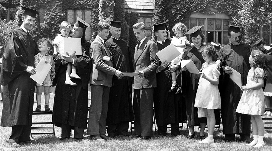 Black and white photo of men and women in caps and gowns posing with children