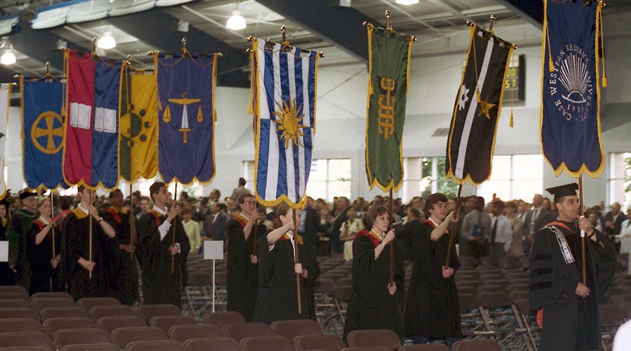 A photo taken indoors at CWRU as graduates hold heraldic banners from each of the university's schools