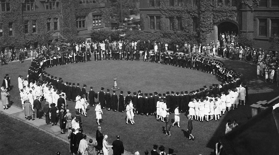 Black and white photo taken from above of women gathered in a circle around a sundial on a green space on campus