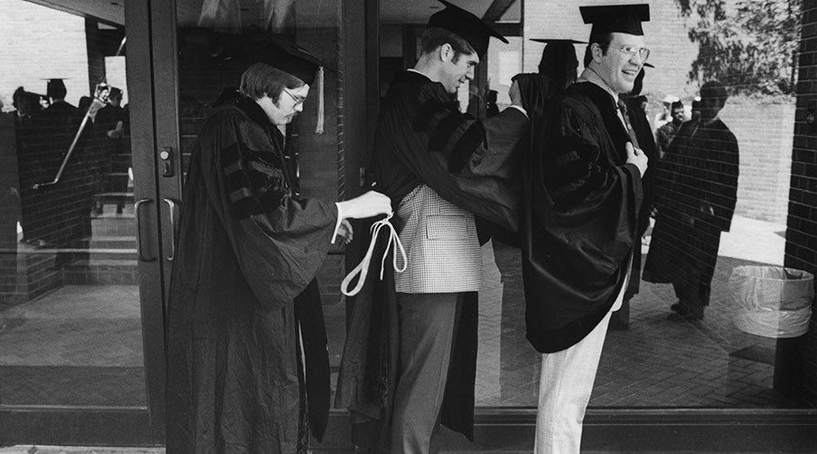 Black and white image of three men standing together helping each other adjust their academic robes
