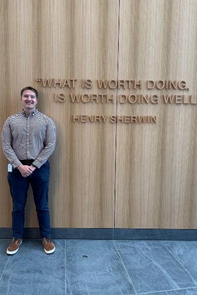 Connor Black standing in front of a mural that says "What is worth doing is worth doing well" by Henry Sherwin