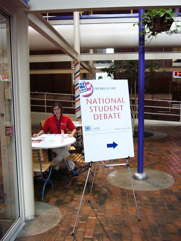 Photo of a student sitting in Thwing Center next to a sign that says "National Student Debate"