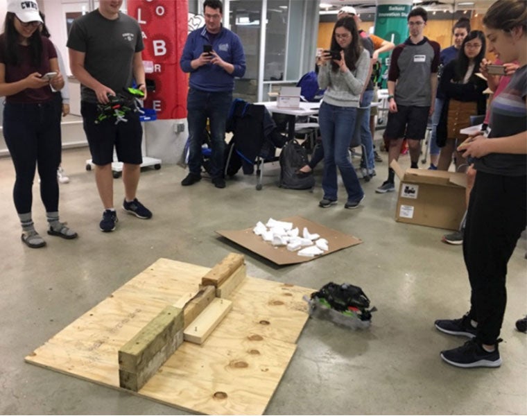Case School of Engineering students stand around a small robotic vehicle and watch it try to climb over a block of wood