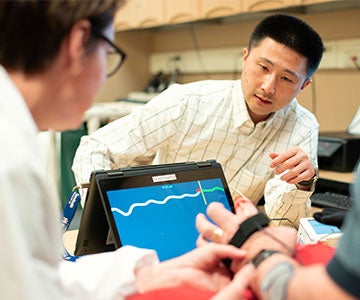 Assistant professor Michael Fu works with a patient who is wearing a band on his hand to measure muscle activity