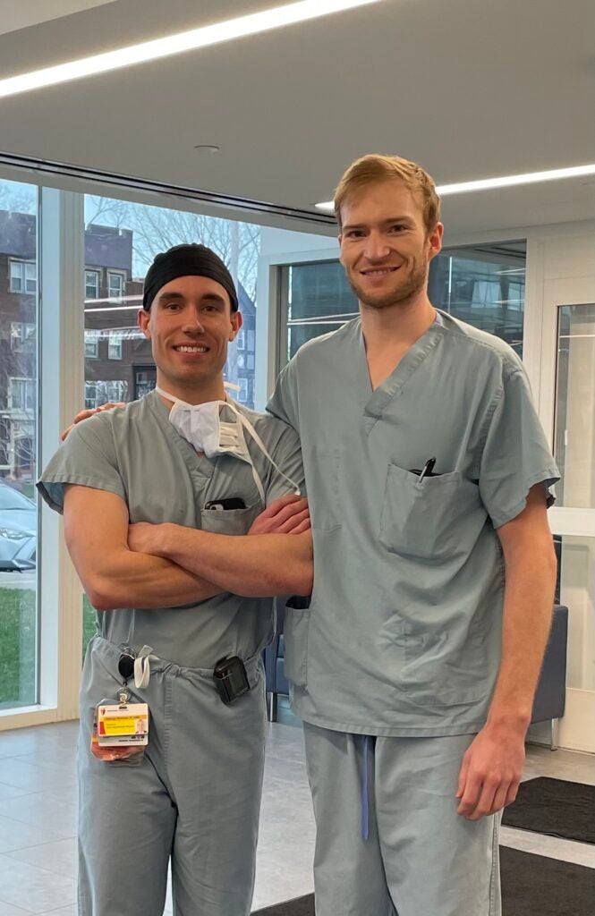 Dental residents George Schieder and Kyle Baird pose in the clinic wearing scrubs.