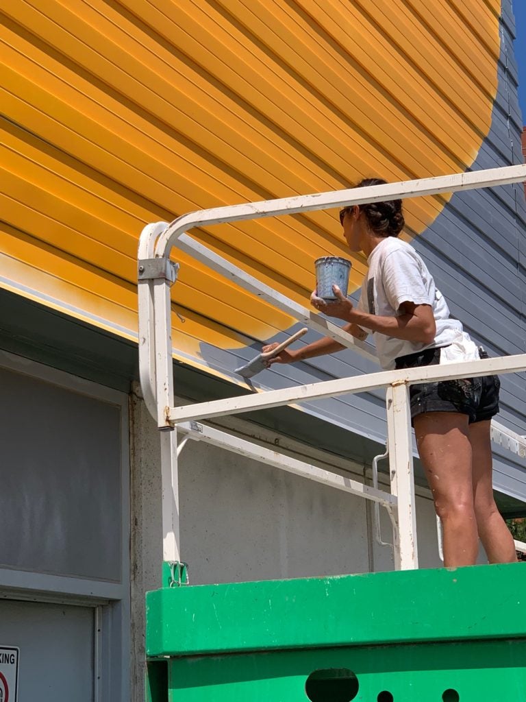 Artist on a scaffold painting a wall mural. 