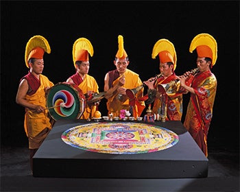 Tibetan monks playing instruments around a sand mandala