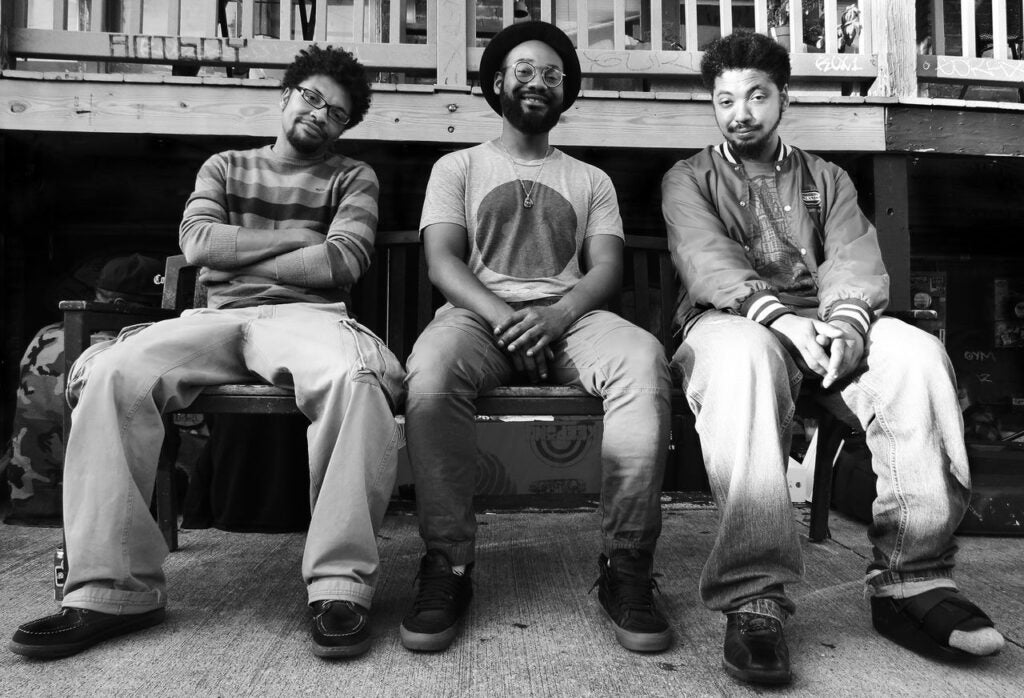 Black and white photo of the three members of Muamin Collective sitting on a bench