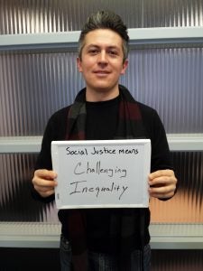 John Flores holding sign that says "Social justice means challenging inequality"