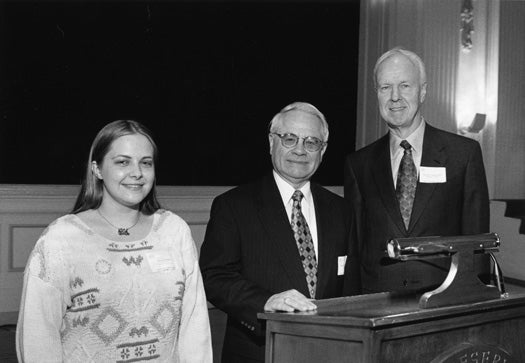 Richard Zdanis stands at a podium and poses for a photo with a woman and David Auston