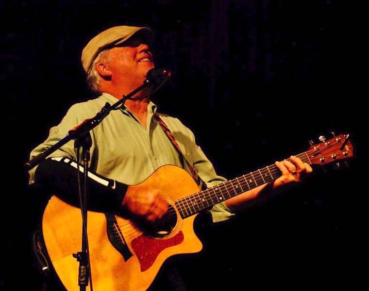 Photo of Alex Bevan singing into a microphone and playing guitar