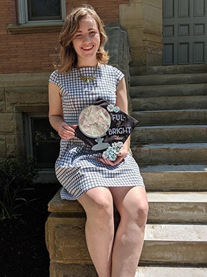 Photo of Anna Sklenar holding her grad cap, which says "Ful- of bright ideas"
