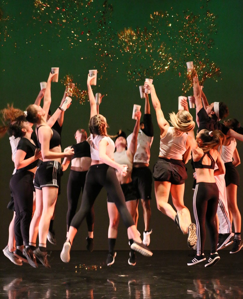 Photo of a group of dancers jumping in a circle while holding cups with confetti coming out