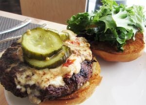 Burger on plate with cheese and pickles with top of bun next to it with lettuce