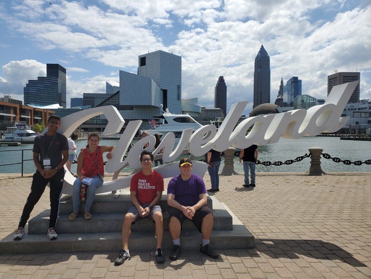 Four members of the Class of 2023 pose with the Cleveland sign with the Rock and Roll Hall of Fame and skyline in the background