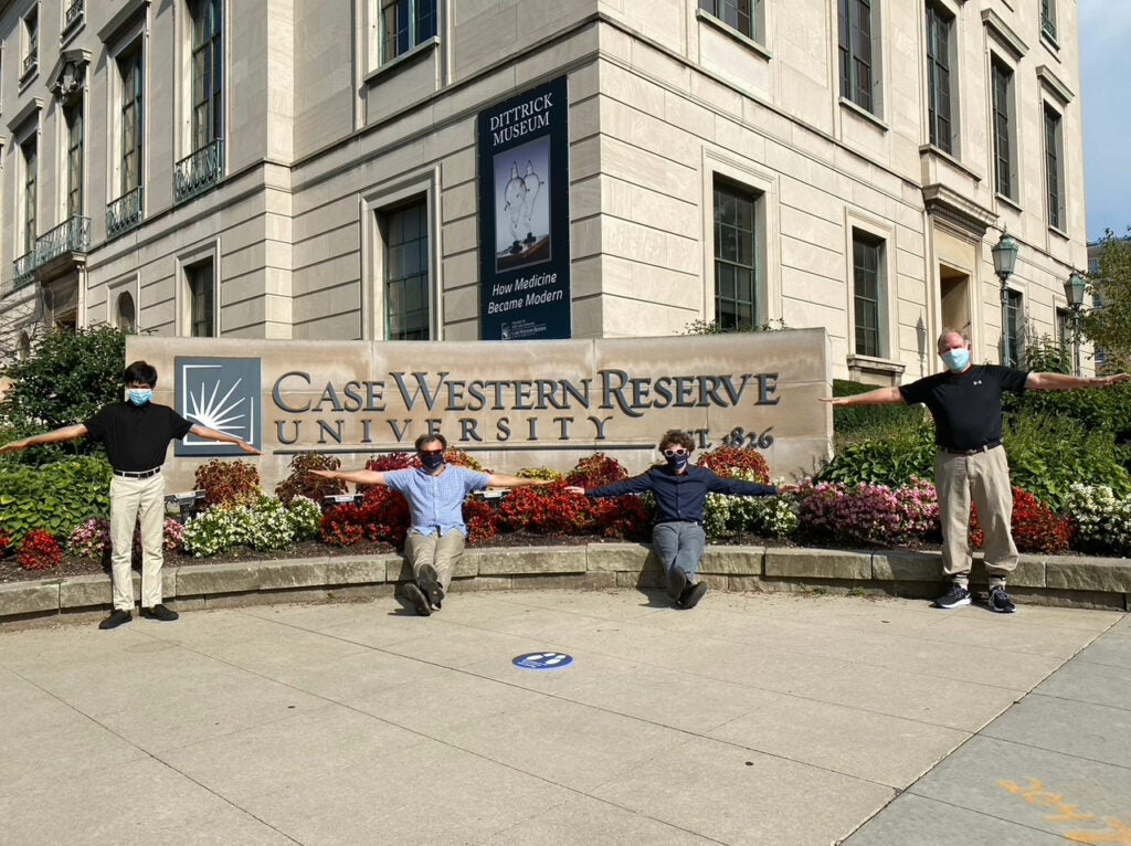 Photo of the COVID-19 Predict team in front of CWRU sign holding their hands out to socially distance and wearing masks