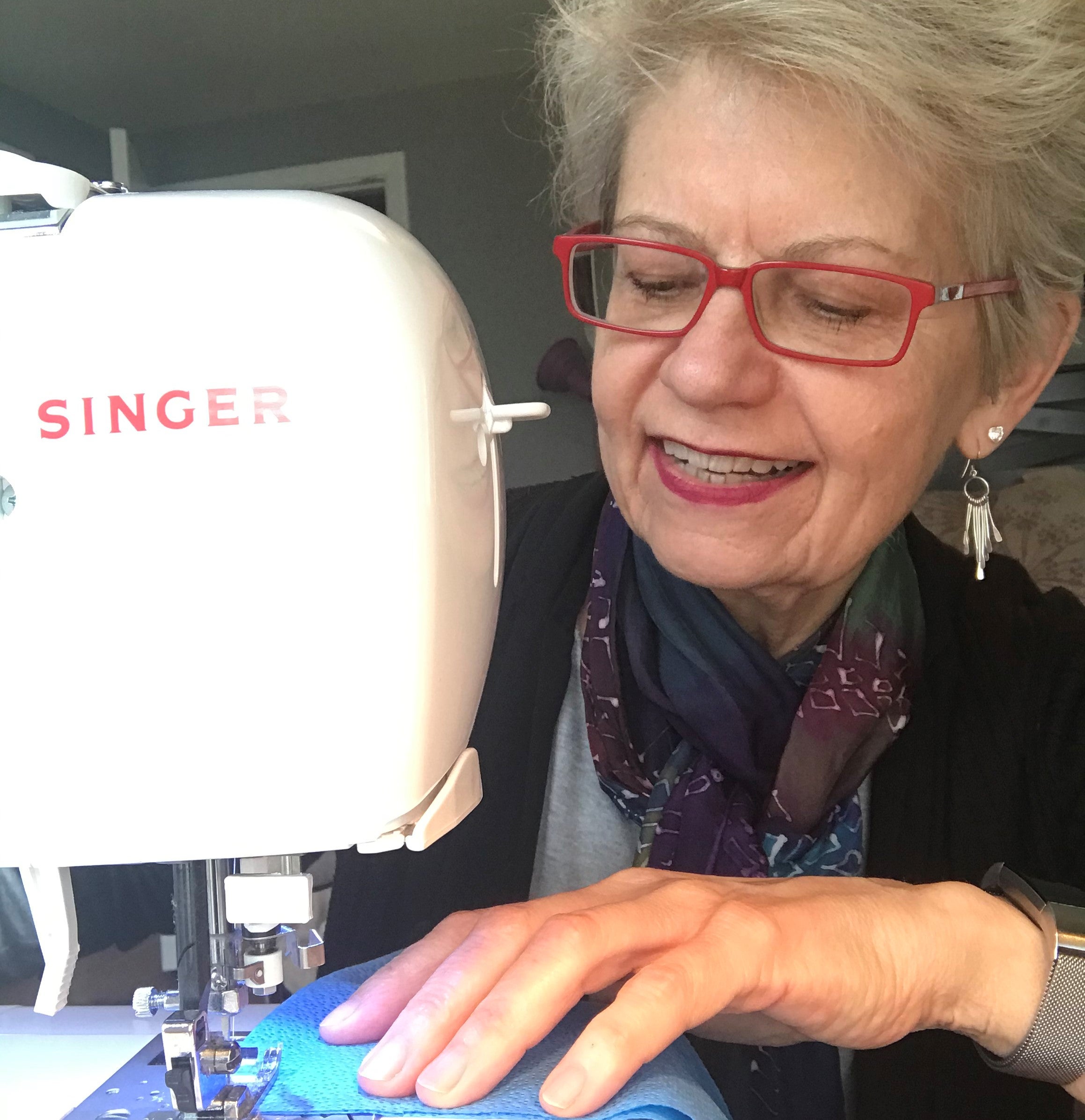 A smiling Dr. Jasinevicius uses a sewing machine to sew a mask.