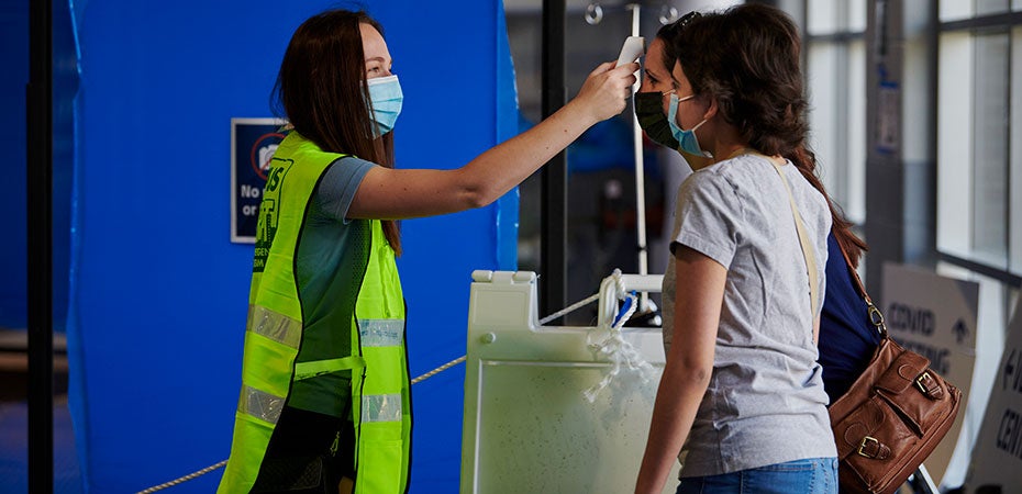 A COVID-19 test site volunteer takes the temperature of attendees.
