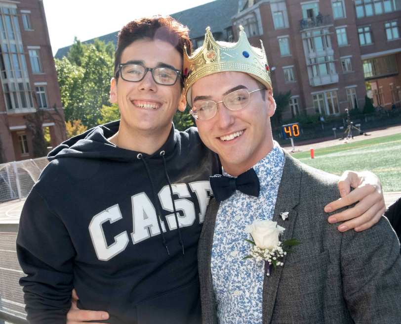 Photo of Adrian in a Homecoming crown and suit with another Case student in front of campus