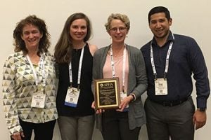 Darcy Freedman poses for photo with APHA staff members while holding award