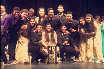 Photo of the Dhamakapella team posing for a photo with a trophy