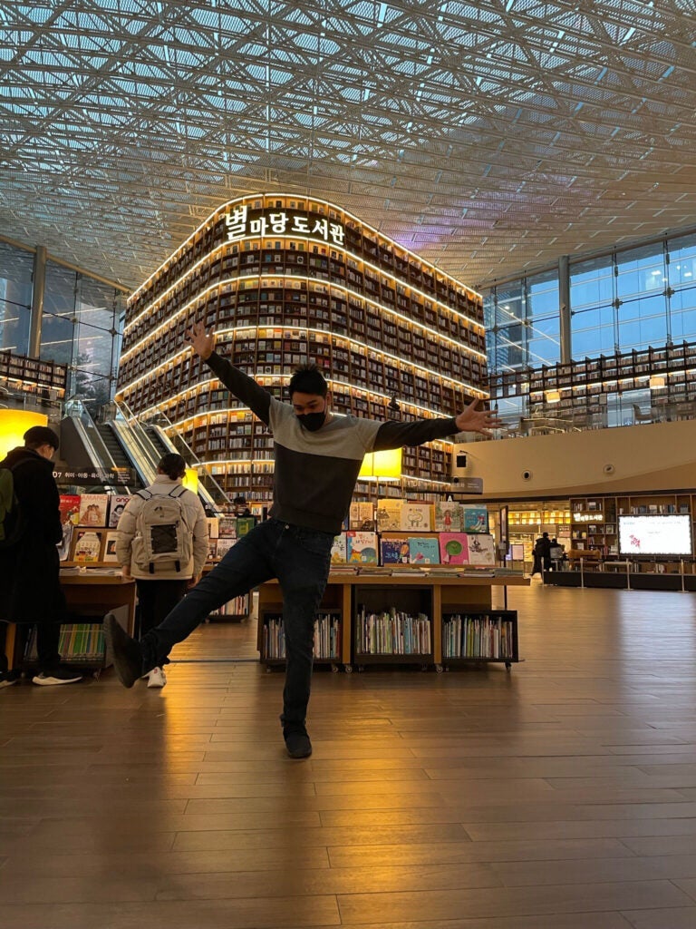 Photo of Elias Tew with his hands and one leg in the air posing in a bookstore in Seoul, South Korea