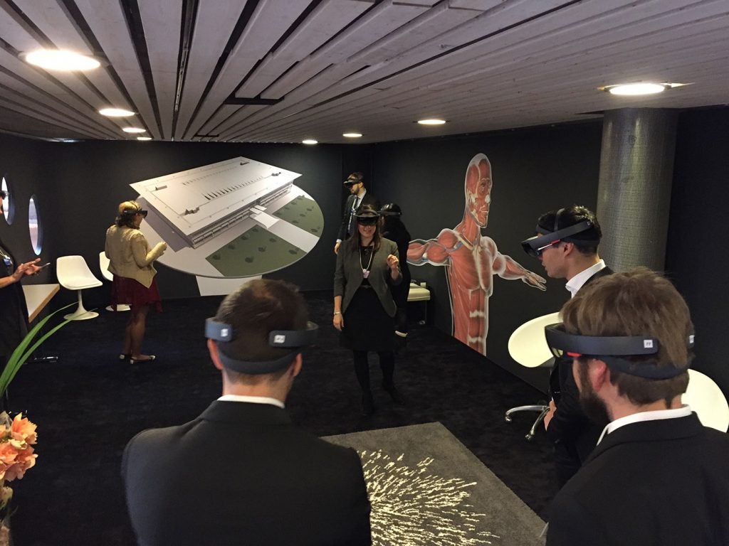People interact with the Interactive Commons exhibit at Congress Centre Davos with Health Education Campus rendering in the background