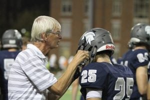 Hugh Marshall helps a CWRU football player with his helmet