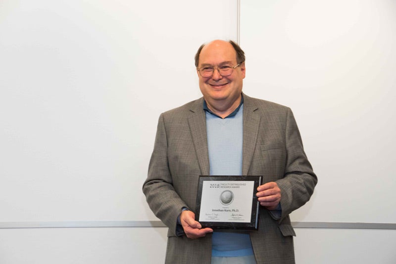 Photo of Jonathan Karn holding Faculty Distinguished Research Award plaque