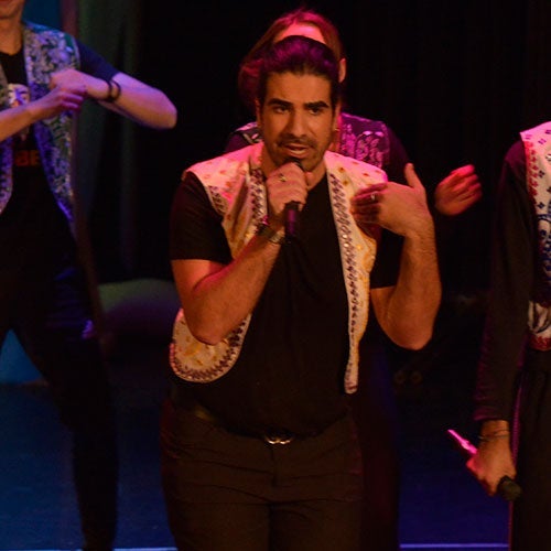 Photo of Matt Loria singing into a microphone on stage during a production