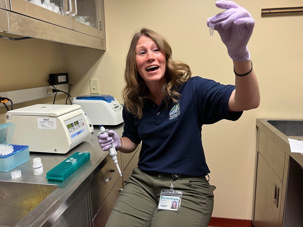 Photo of Maura Plocek smiling as she holds something up while working in the lab