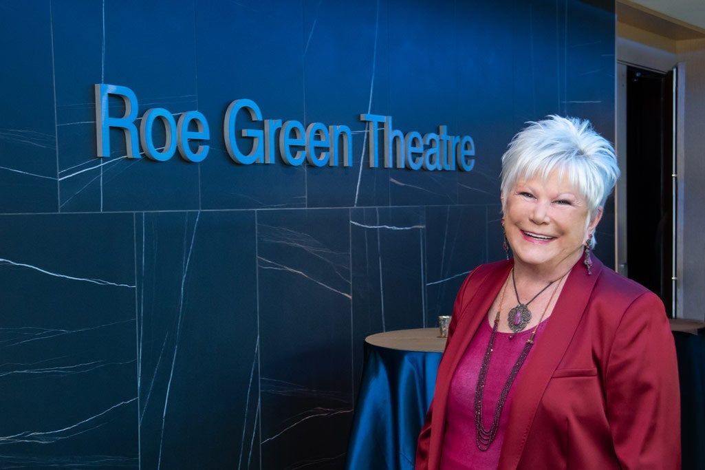 Photo of Roe Green in front of signage that says "Roe Green Theatre"