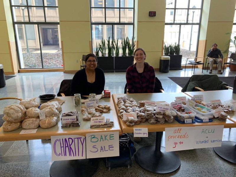 Two female students sitting at a table running a bake sale