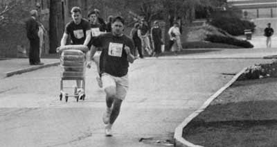 Black and white photo of students participating in a Spring Olympics event with students running, one with a shopping cart