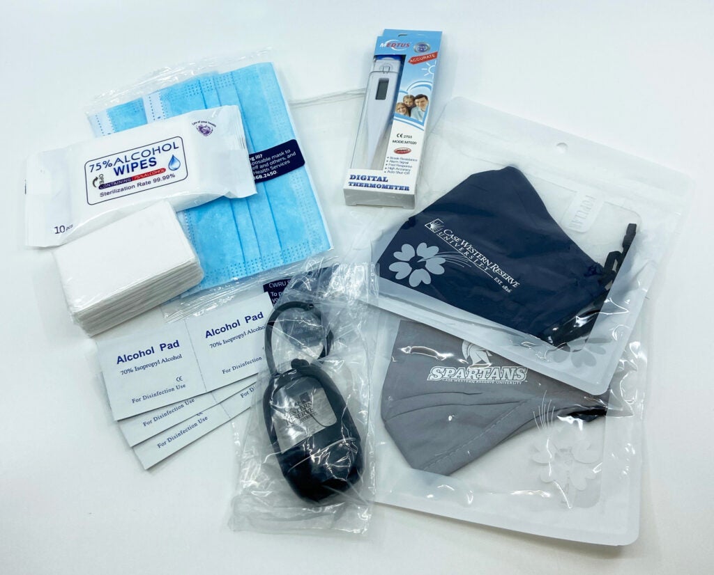 Photo of hand sanitizer, cloth masks, surgical masks, a thermometer and sanitizing wipes on a table