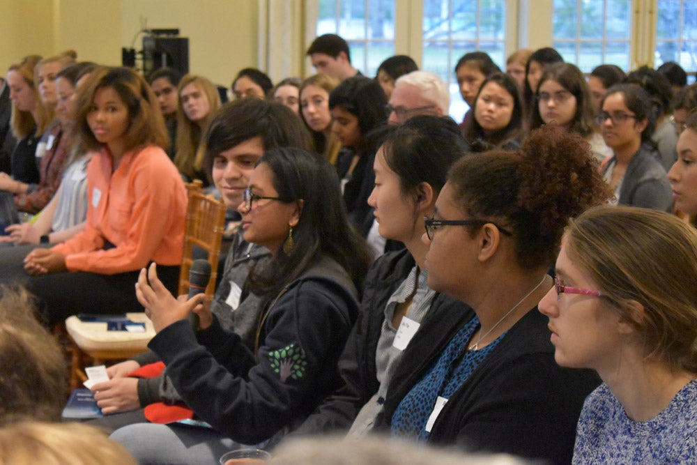 Photo of a woman holding a microphone surrounded by an audience of mostly women at a Women in Tech Initiative event