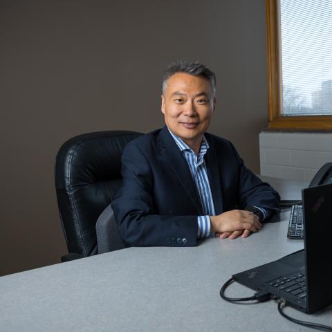 Photo of person sitting at desk with computers, smiling at camera