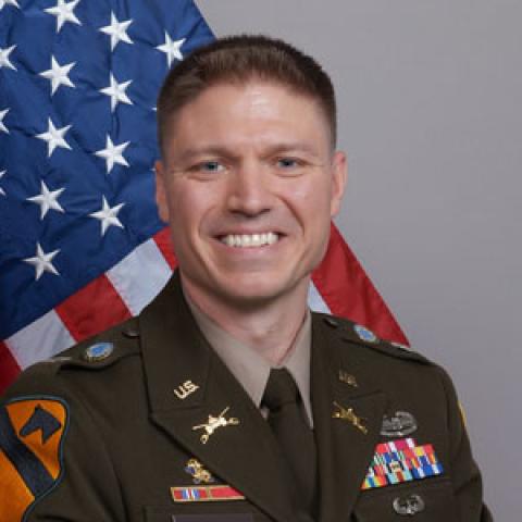 Person wearing military uniform, smiling in front of American flag