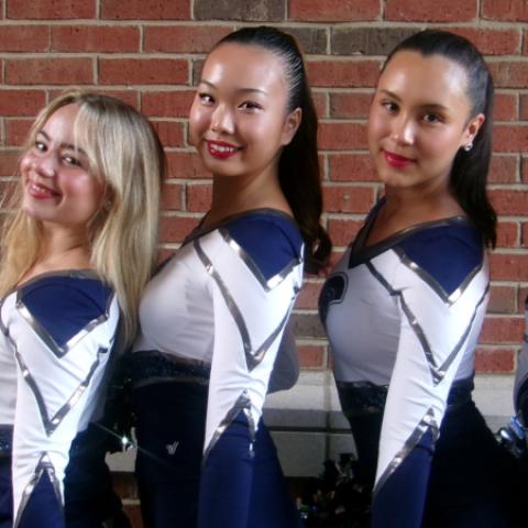 Four members of the CWRU Dance Team pose in their uniforms in front of a brick wall.